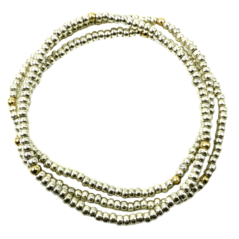 A stack of three bracelets, featuring a pattern of platinum with gold-filled beads, laid out on a white surface.