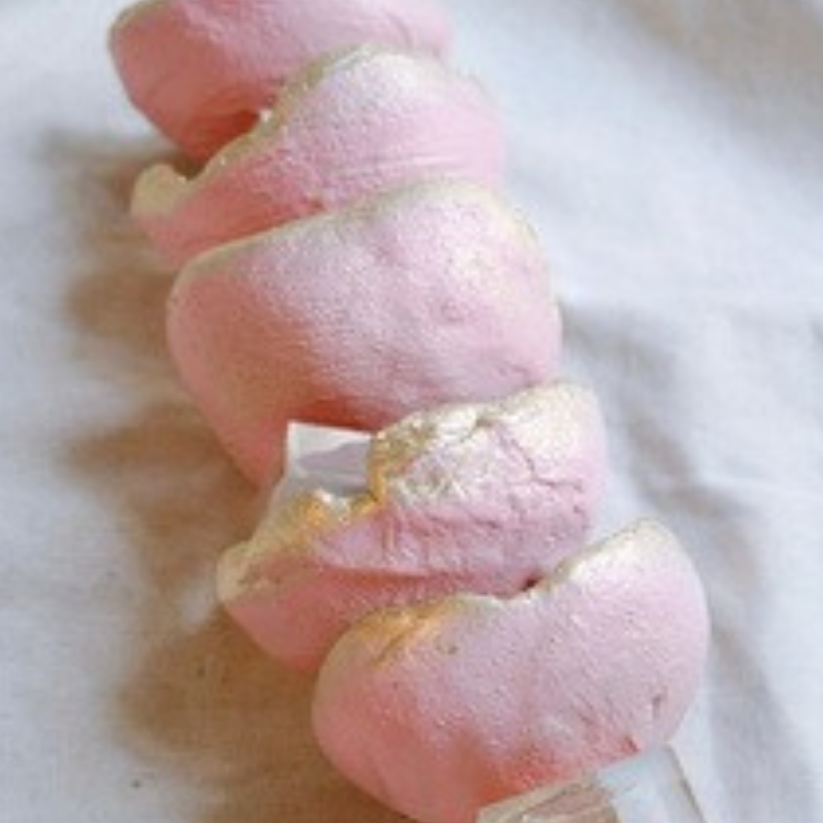 A close-up of a spiral-shaped pink pastry or marshmallow treat on a white surface.