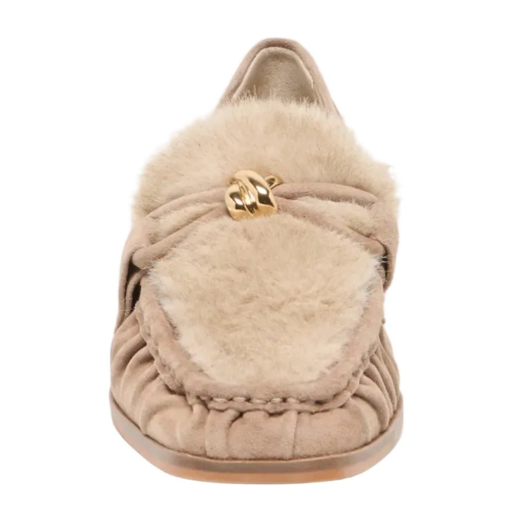 A single beige slip-on moccasin-style shoe with a fluffy shearling-style collar and a small gold-tone decorative accent on the front, shown against a light gray background.