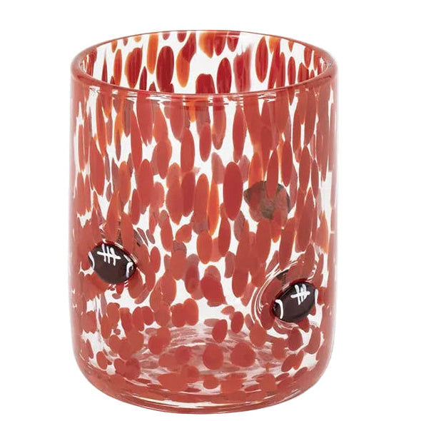 A clear glass tumbler featuring a red and orange speckled pattern and two small football-shaped cutouts on the front, set against a plain white background.