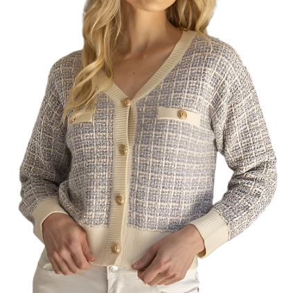A female model wearing a beige and purple tweed cardigan with a V-neck and cream banding, paired with white pants.