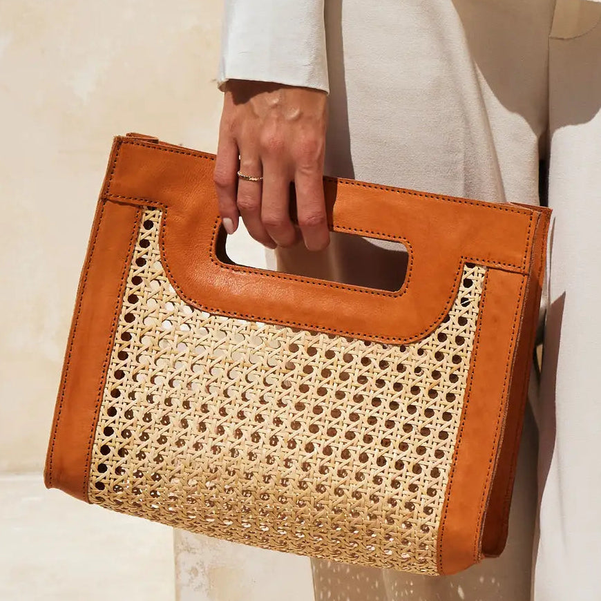 Brown handbag with woven design held by a person against a neutral background