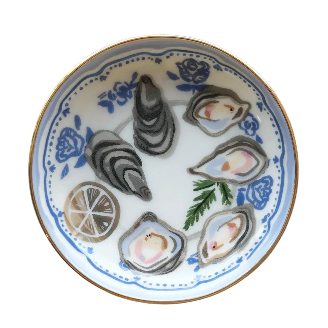 A round ceramic plate with a white base, decorated with blue floral patterns, illustrated oysters, a lemon slice, and a green herb sprig, finished with a gold rim, shown from a top-down view on a light marble surface.