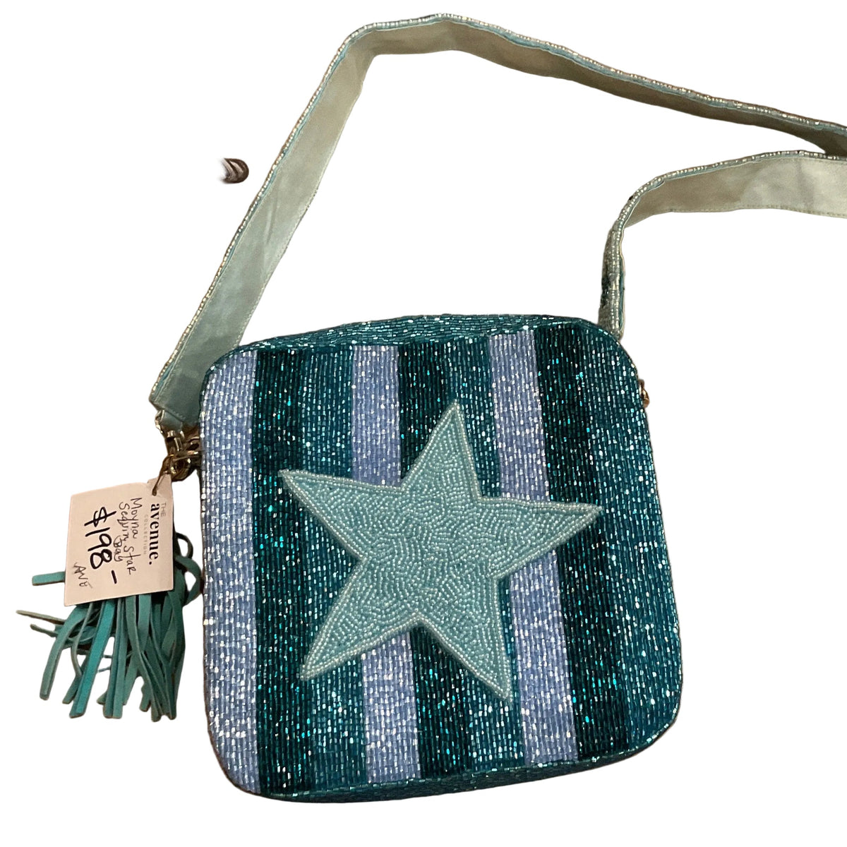 A handmade crossbody bag with a glittery blue and purple striped pattern and a central light blue star applique, displayed on a wooden table with Kravet accessories.