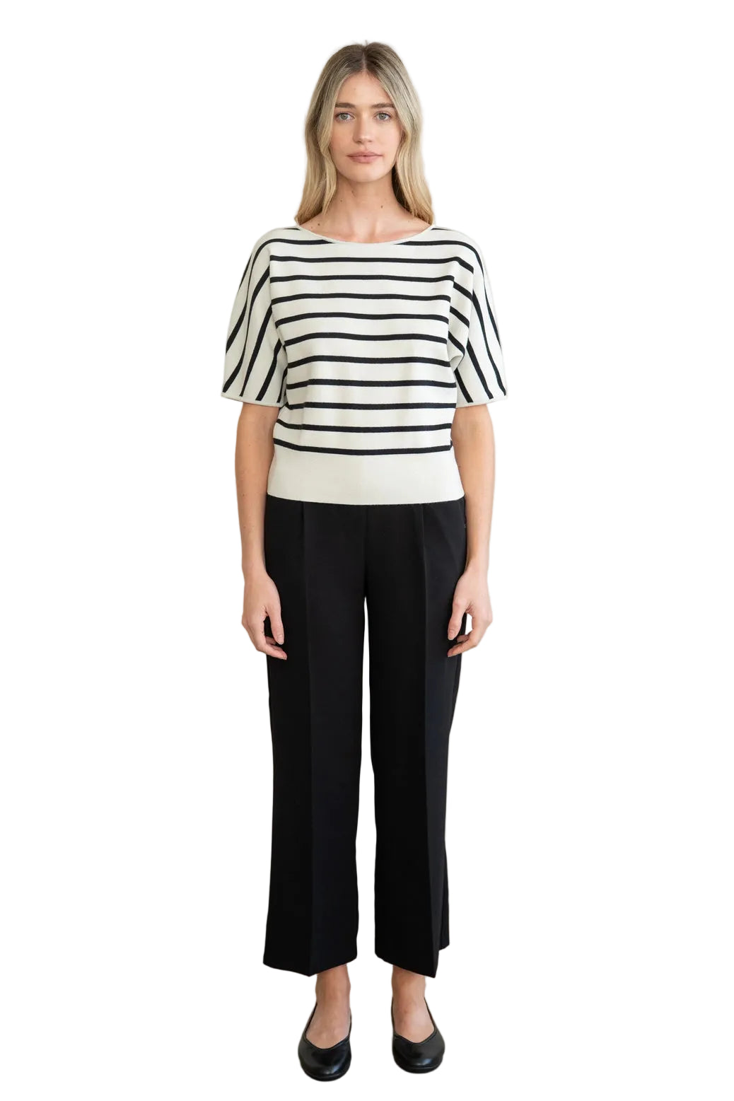 A woman modeling a short-sleeve knit top with black horizontal stripes on an off-white background, paired with black wide-leg cropped pants and black flats, standing against a neutral beige wall.