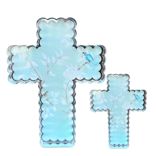 Two light blue cross-shaped decorative items with scalloped edges, featuring a floral branch pattern and small bird motifs, shown on a plain white background.