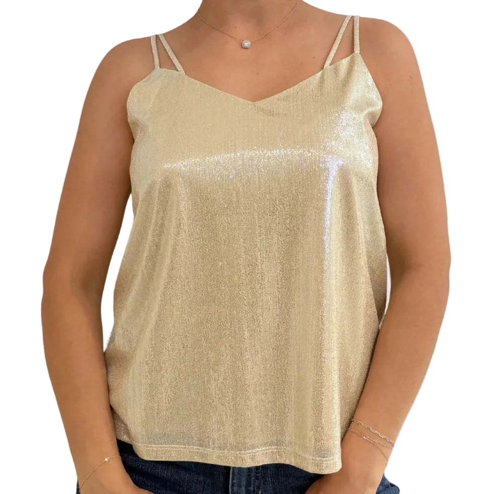 A woman wearing a shimmering metallic champagne-gold spaghetti-strap tank top and blue jeans, shown from the neck down against a light gray studio background.