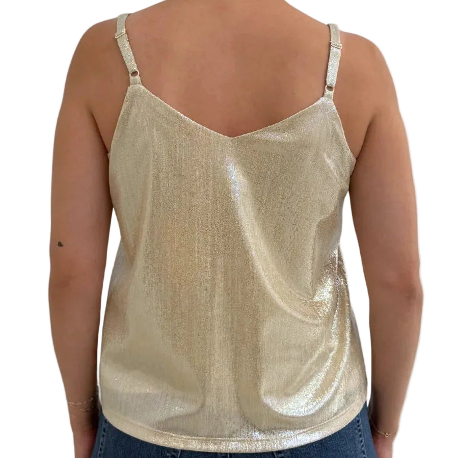A woman viewed from the back wearing a shiny metallic champagne-gold spaghetti-strap tank top and dark blue jeans, against a light gray studio background.