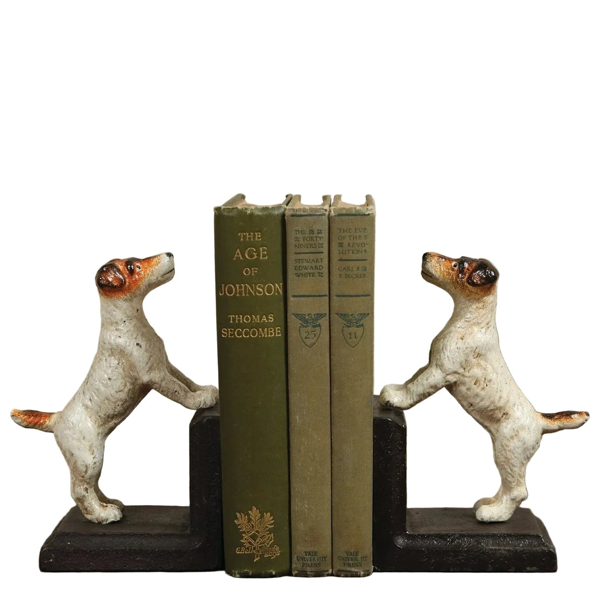 A pair of dog-shaped bookends holding up three vintage green books on a wooden surface against a textured beige wall. The bookends are white with orange and black markings, standing on dark bases.