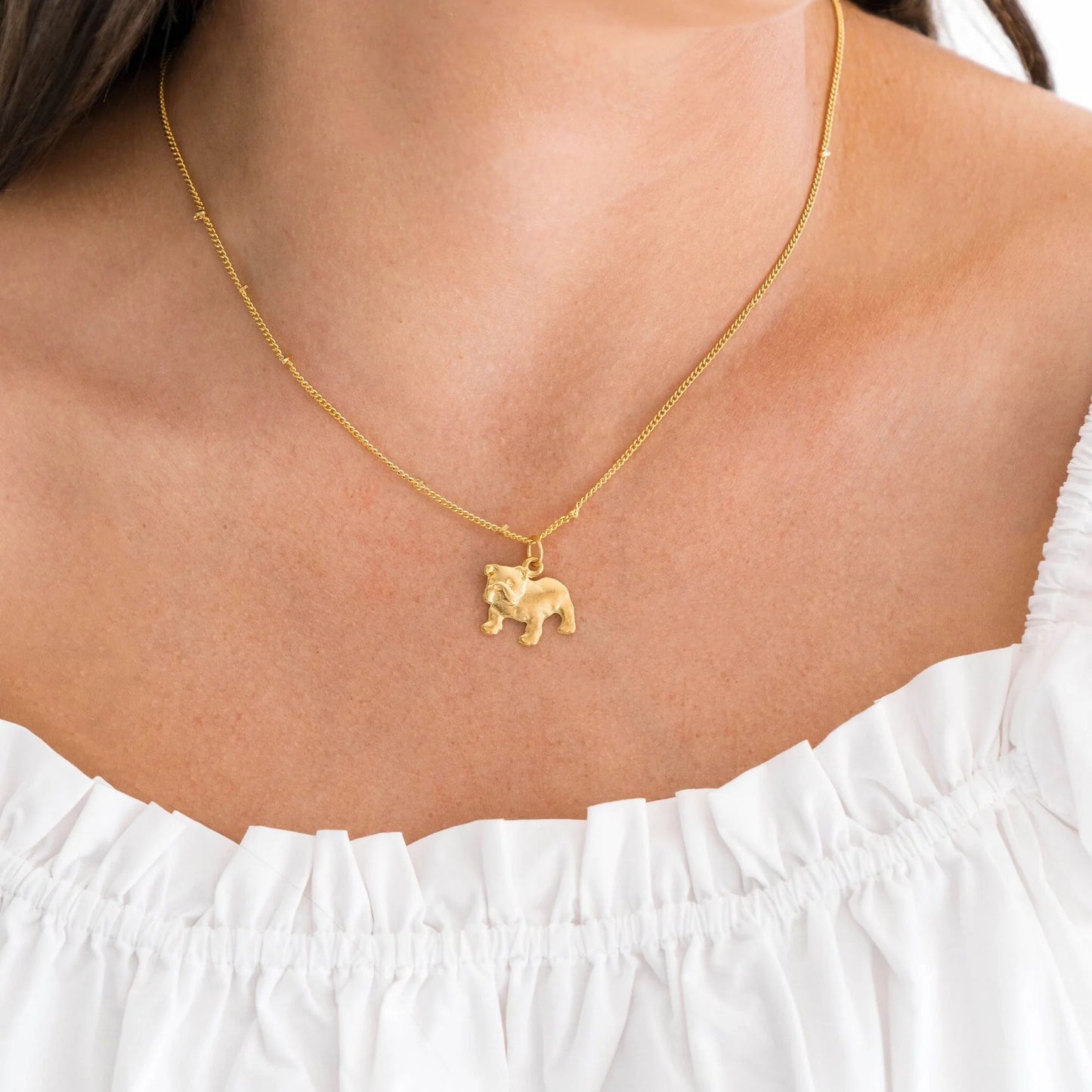 Gold necklace with a small pendant worn by a person in a white top