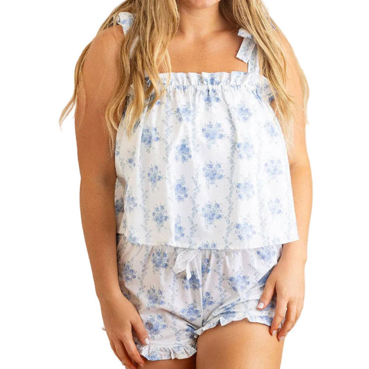 A woman modeling a matching two-piece sleepwear set featuring a white top and shorts with a light blue floral pattern, set against a plain white background.