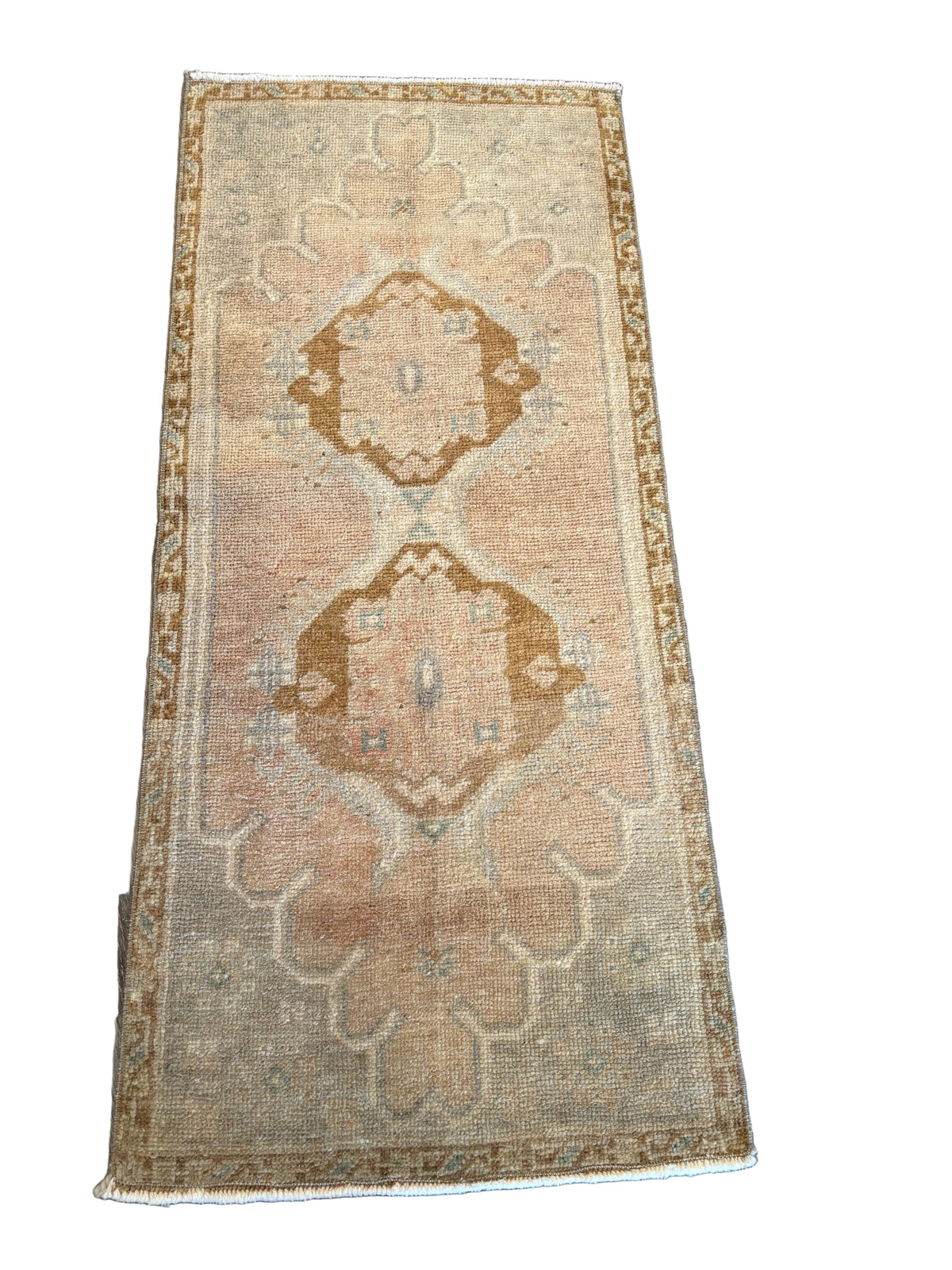 A rectangular vintage-style area rug with a distressed beige and brown geometric pattern, laid flat on a dark wood plank floor.