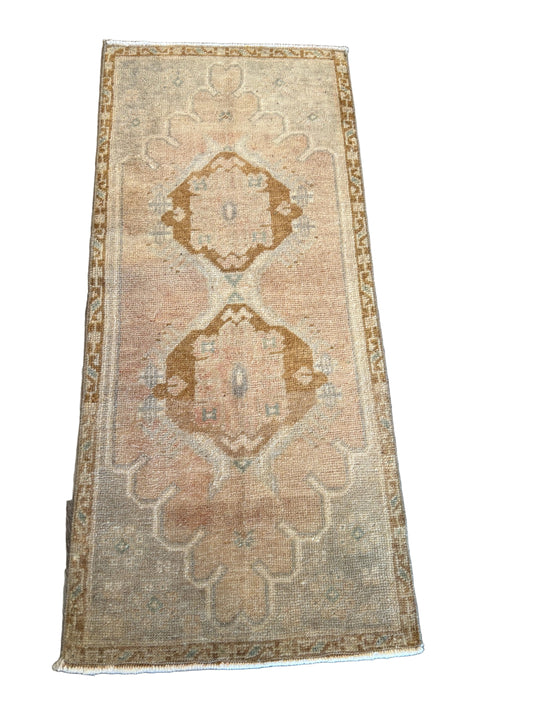 A rectangular vintage-style area rug with a distressed beige and brown geometric pattern, laid flat on a dark wood plank floor.