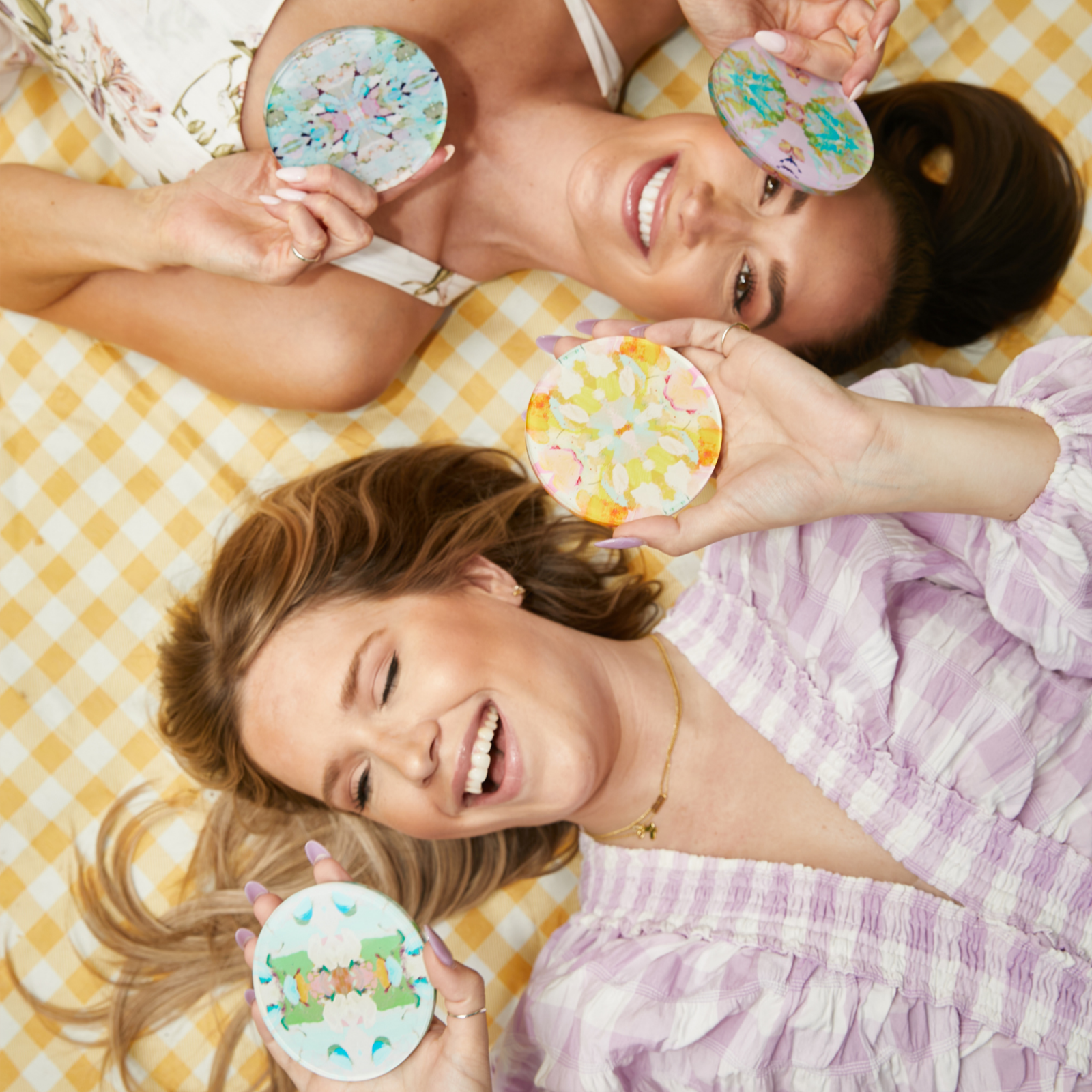 Two women lying on a checkered blanket holding decorative circular objects.