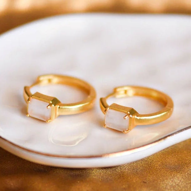 Gold hoop earrings on a white dish with a textured brown surface underneath