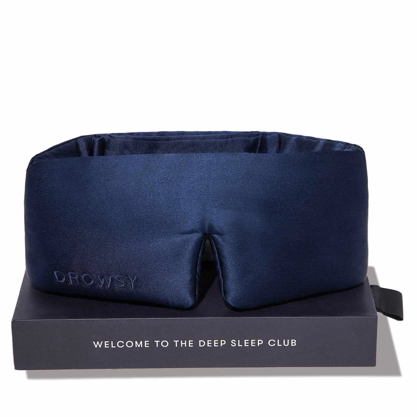 A navy blue satin sleep mask resting on a dark gray presentation box with the text 'WELCOME TO THE DEEP SLEEP CLUB'. The brand name 'PROLEY' is subtly debossed on the left side of the mask.