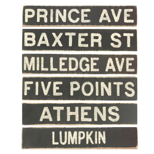 A set of six vintage-style street sign plaques with black backgrounds and cream lettering, reading 'PRINCE AVE', 'BAXTER ST', 'MILLEDGE AVE', 'FIVE POINTS', 'ATHENS', and 'LUMPKIN'.