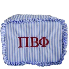 A blue and white striped pillow with ruffled trim and red Greek letters 'ΠBΦ' on the front, resting on a beige couch in front of a white paneled wall.