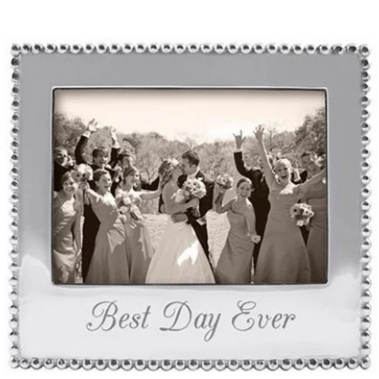 A square silver-toned photo frame with a beaded border and the words 'Best Day Ever' printed at the bottom, holding a black-and-white wedding photograph of a bride and groom with bridesmaids and guests.