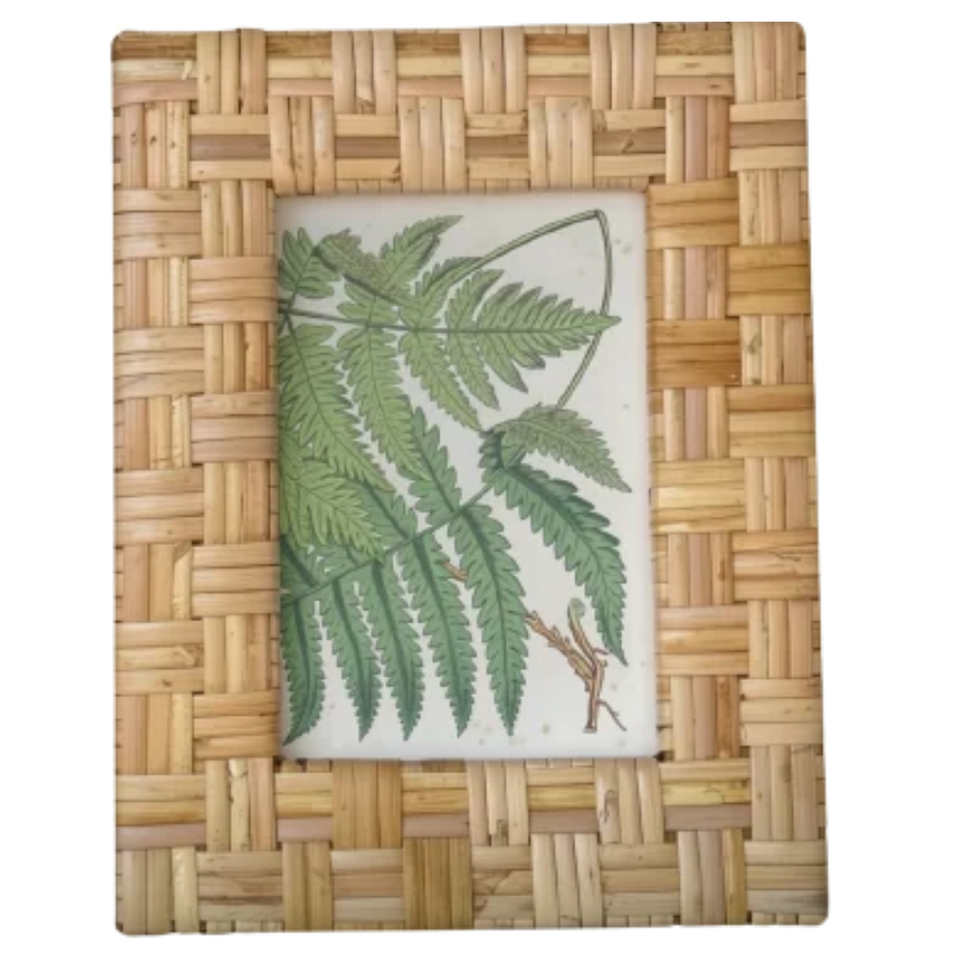 A square decorative picture frame with a woven natural rattan border and a central botanical print of green fern leaves on a white background.