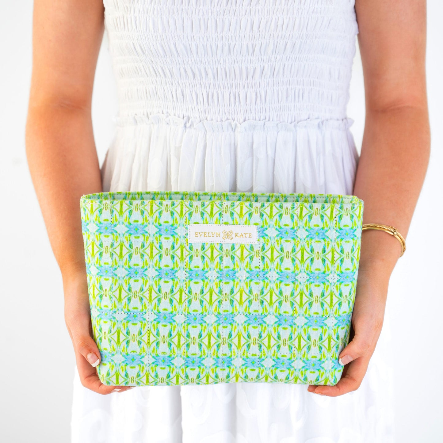 Person holding a green and blue patterned pouch with Evelyn + Kate branding.