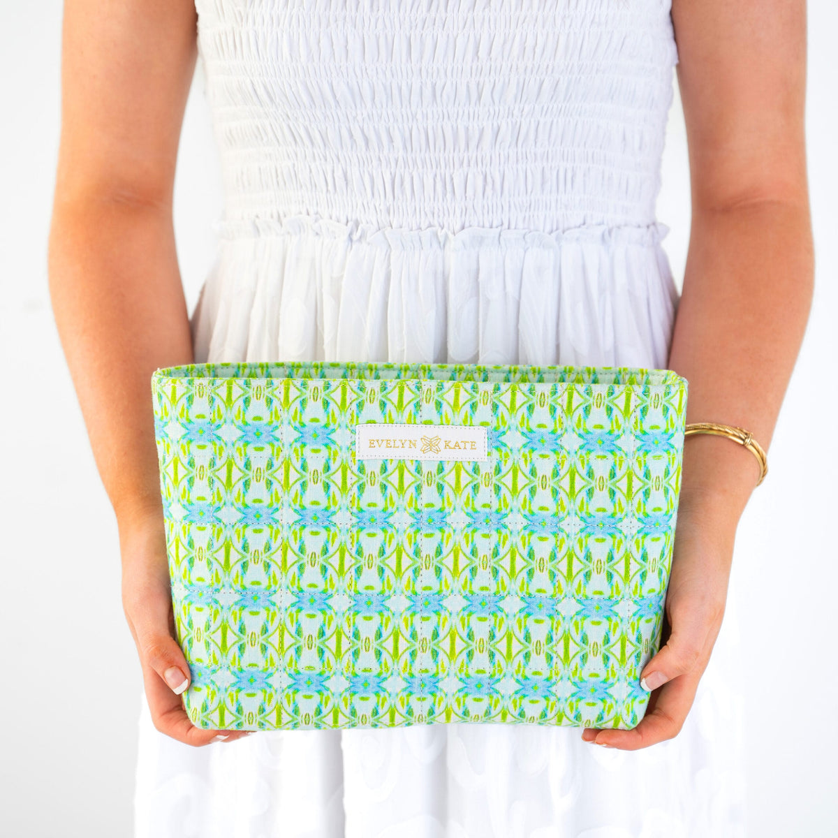Person holding a green and blue patterned pouch with Evelyn + Kate branding.