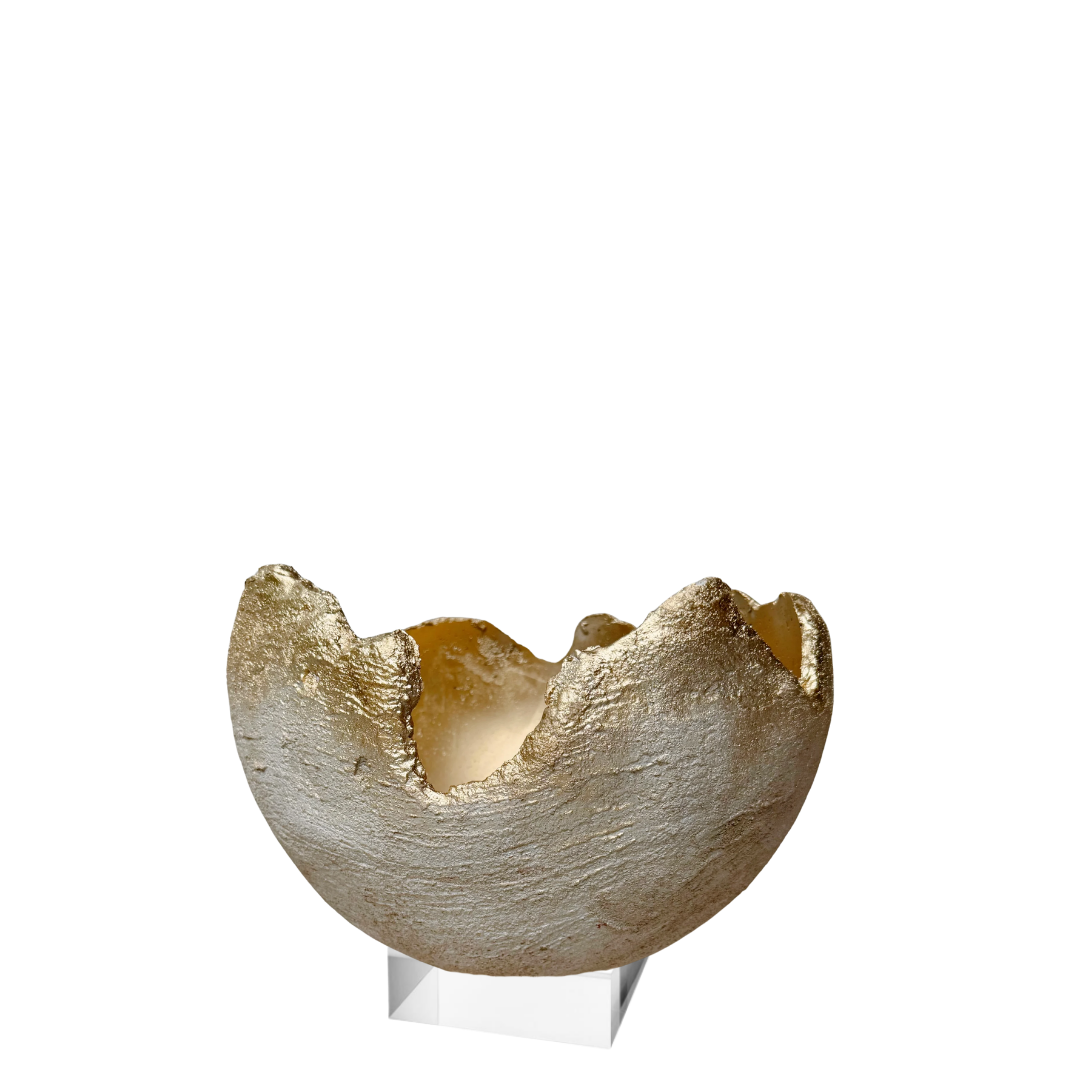 A small sculptural bowl or dish with a textured metallic gold and silver finish, displayed on a clear acrylic stand against a plain white background.