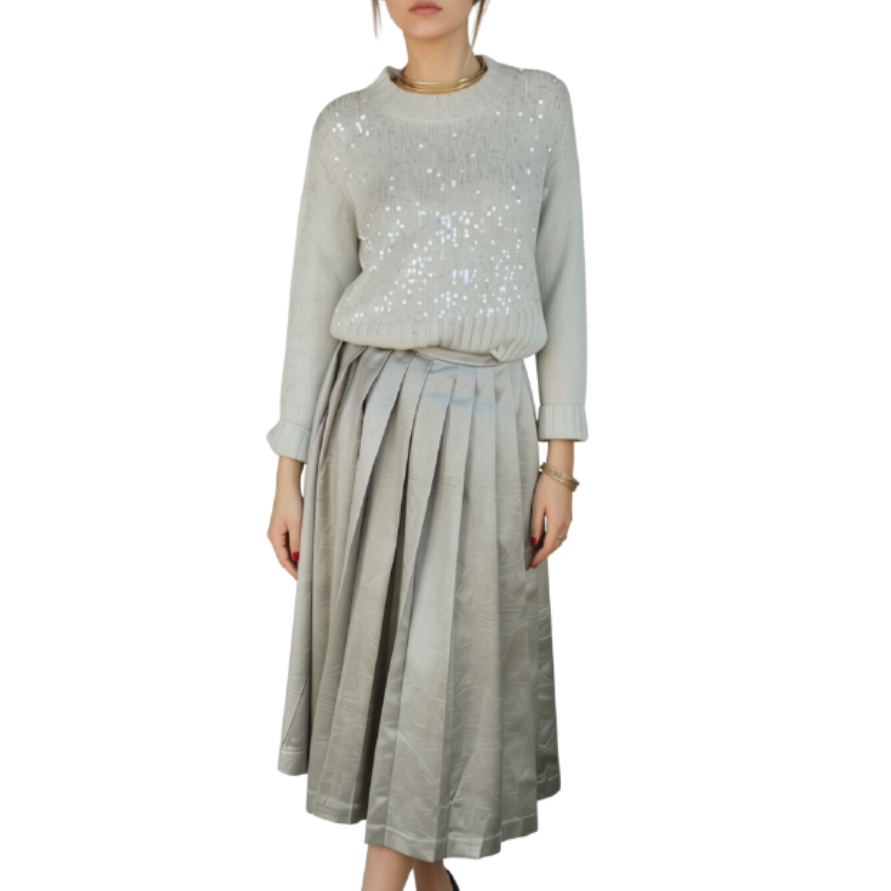 A model wearing a light gray long-sleeve knit top with silver sequins and a matching pleated gray skirt, paired with black sandals, set against a plain white background.