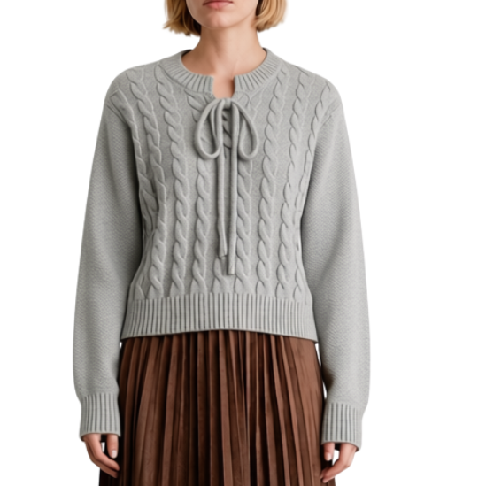 A model stands against a solid white background wearing a light gray cable-knit sweater with a tie detail at the neckline and a brown pleated midi skirt.