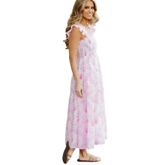 A woman modeling a sleeveless, floor-length white dress with a pink tropical leaf print and ruffled cap sleeves, standing against a solid white background.