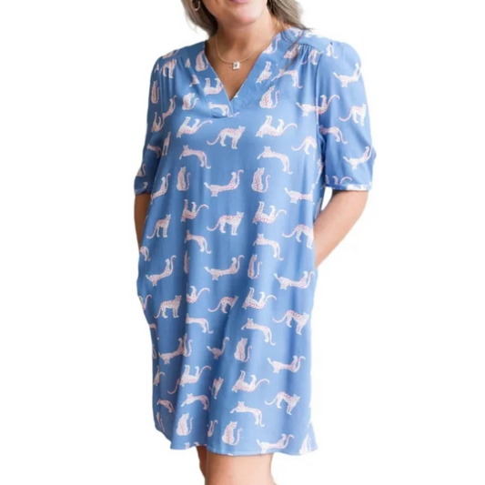 A woman modeling a light blue short-sleeve babydoll dress with a white dalmatian dog print, paired with beige wedge sandals, set against a solid white background.