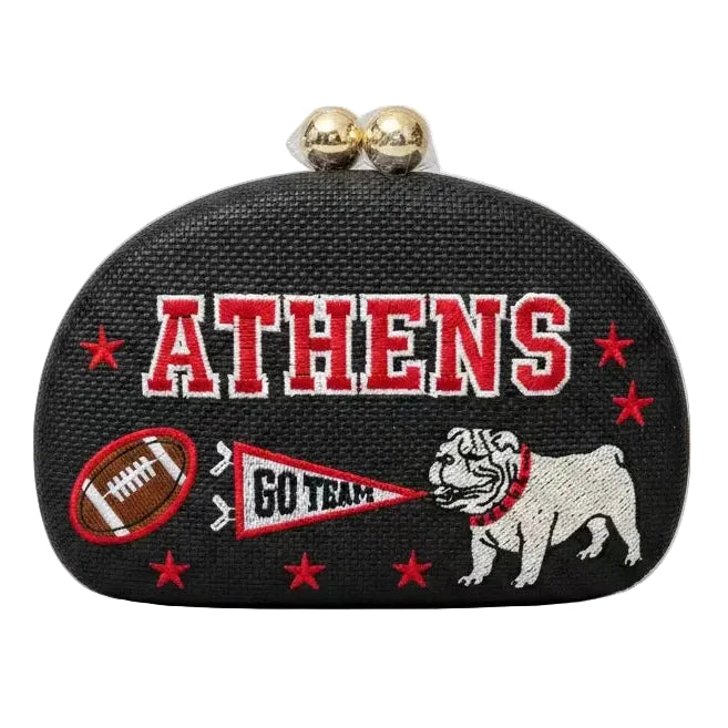A black textured clutch purse featuring embroidered 'ATHENS' in red and white, a bulldog mascot, a football, a pennant reading 'GO TEAM', and red stars, with two gold-tone clasp beads on top, shown against a plain white background.