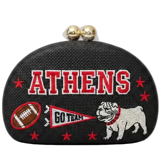 A black textured clutch purse featuring embroidered 'ATHENS' in red and white, a bulldog mascot, a football, a pennant reading 'GO TEAM', and red stars, with two gold-tone clasp beads on top, shown against a plain white background.