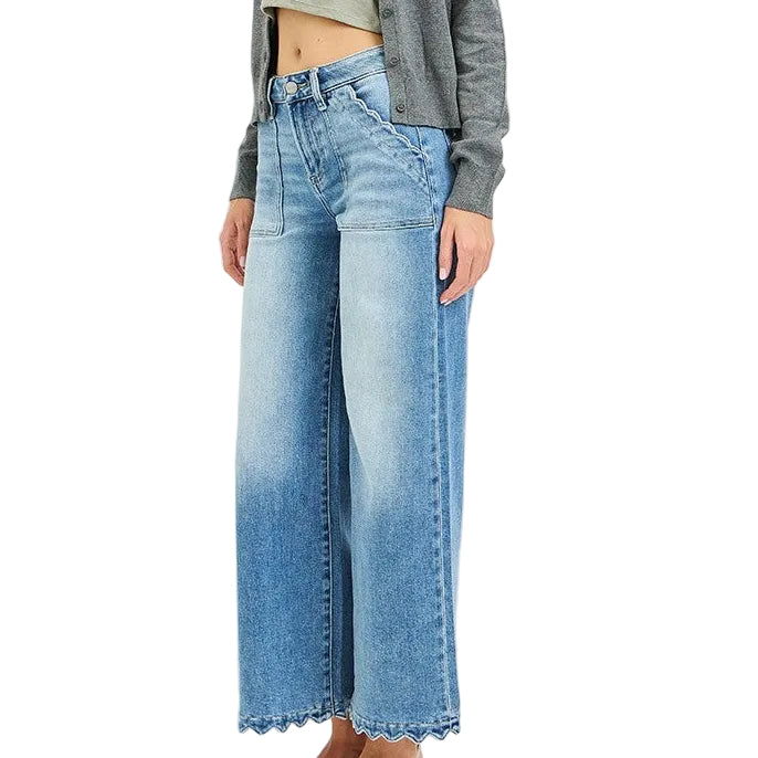 A woman modeling a gray cardigan over a light sage green crop top and wide-leg blue denim jeans with a scalloped hem, paired with gray pointed-toe heels, against a plain white studio background.