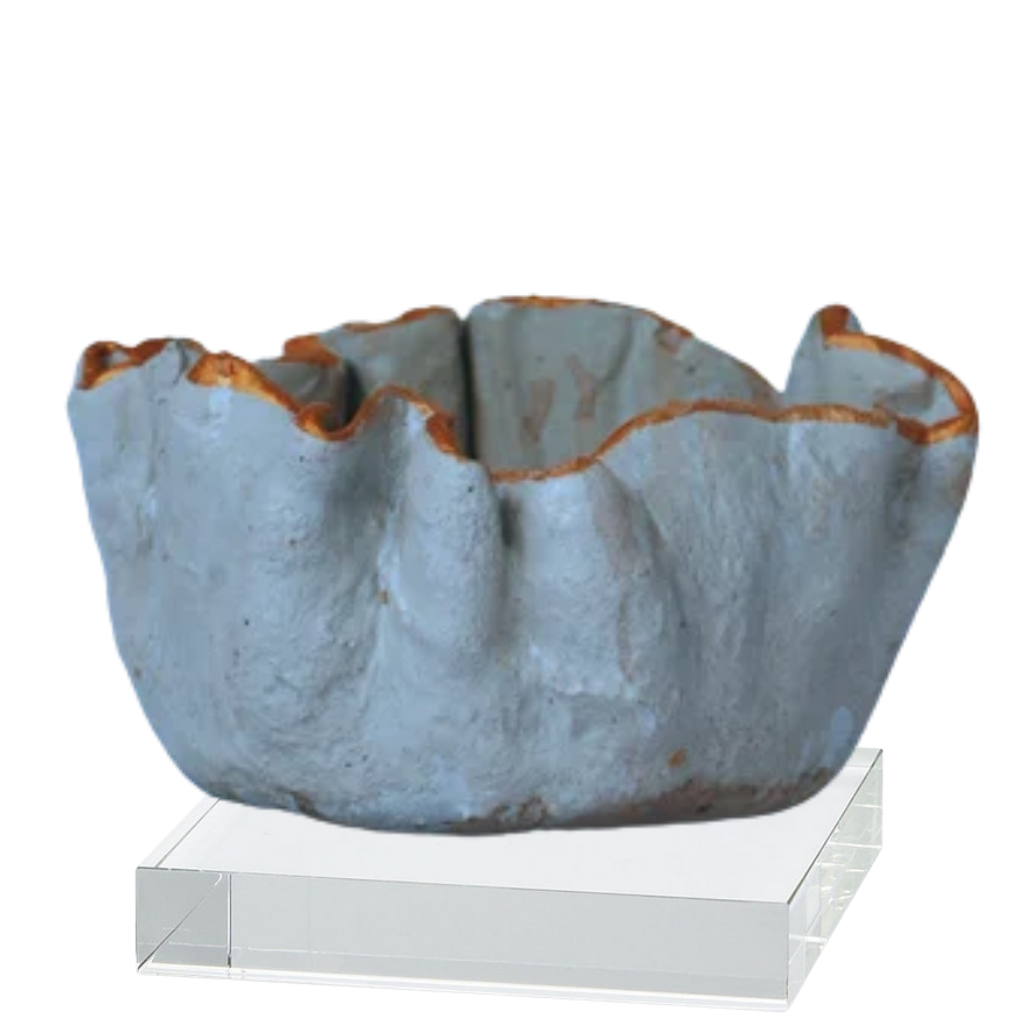 A handmade ceramic bowl with a textured, organic ruffled rim in a dusty blue-gray glaze with brown clay showing at the edges, displayed on a clear acrylic block stand against a white background.