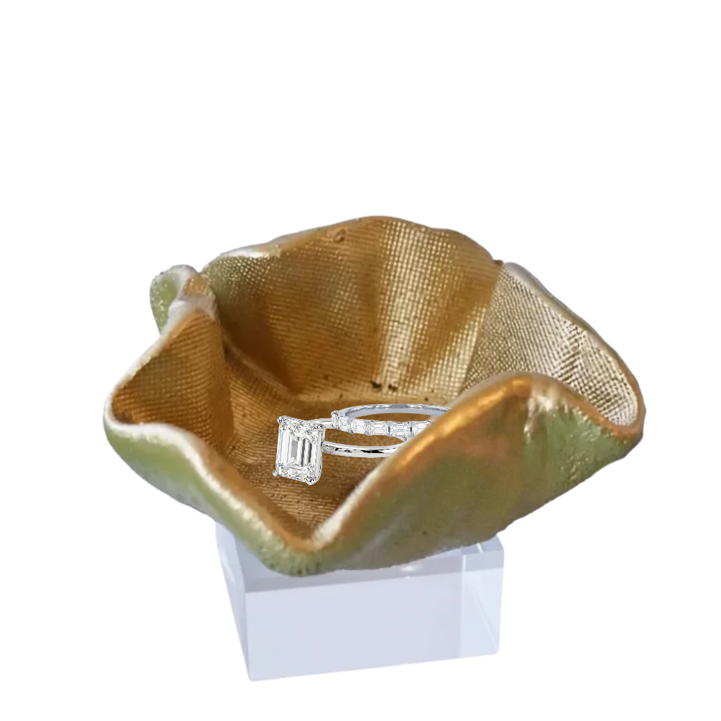 A small sculptural bowl with a wavy, organic shape, featuring a textured metallic gold interior and a greenish-bronze exterior, displayed on a white block stand against a plain white background.