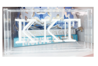 An LED sorority sign with the letters 'KAI' illuminated within a clear acrylic box, mounted on a wall.