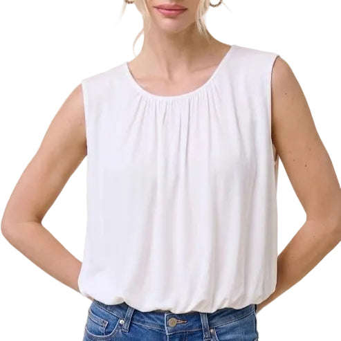 A woman modeling a sleeveless white top with a gathered neckline, paired with blue jeans, against a solid light beige background.