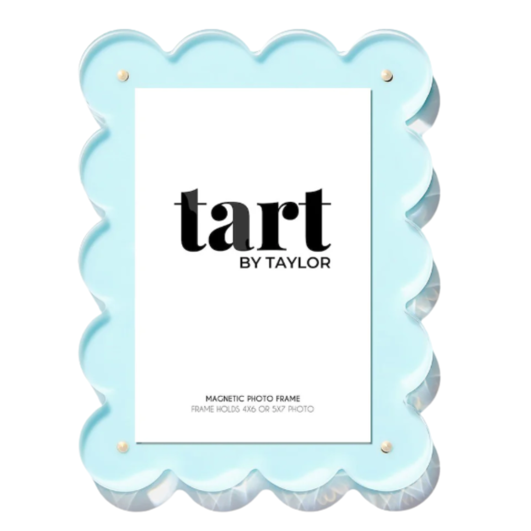 A light blue scalloped magnetic photo frame with gold-tone corner hardware, shown on a plain white background. The frame contains a white insert card with the brand name 'tart BY TAYLOR' printed in black.