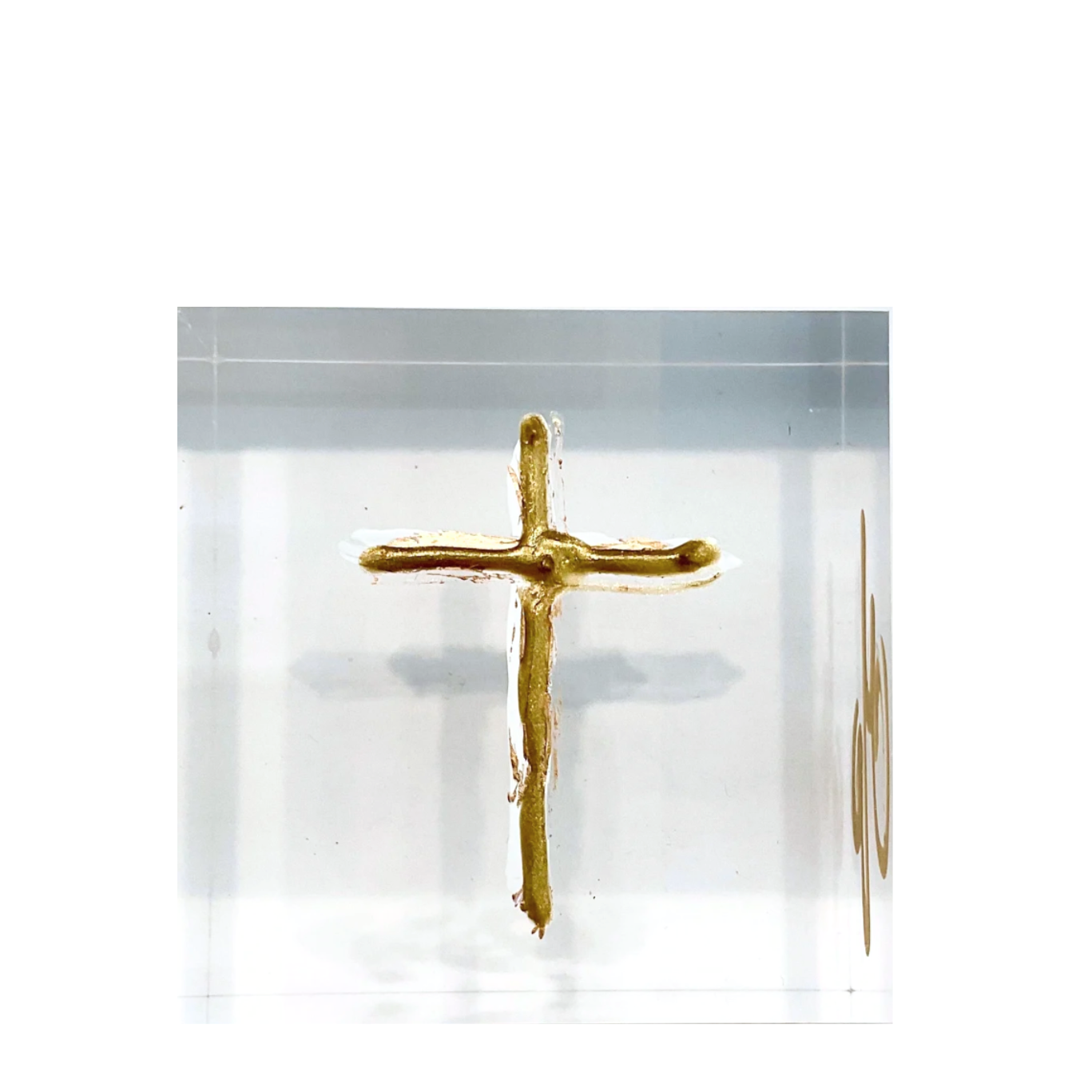 A small gold cross pendant or charm displayed inside a clear square acrylic block on a white background.