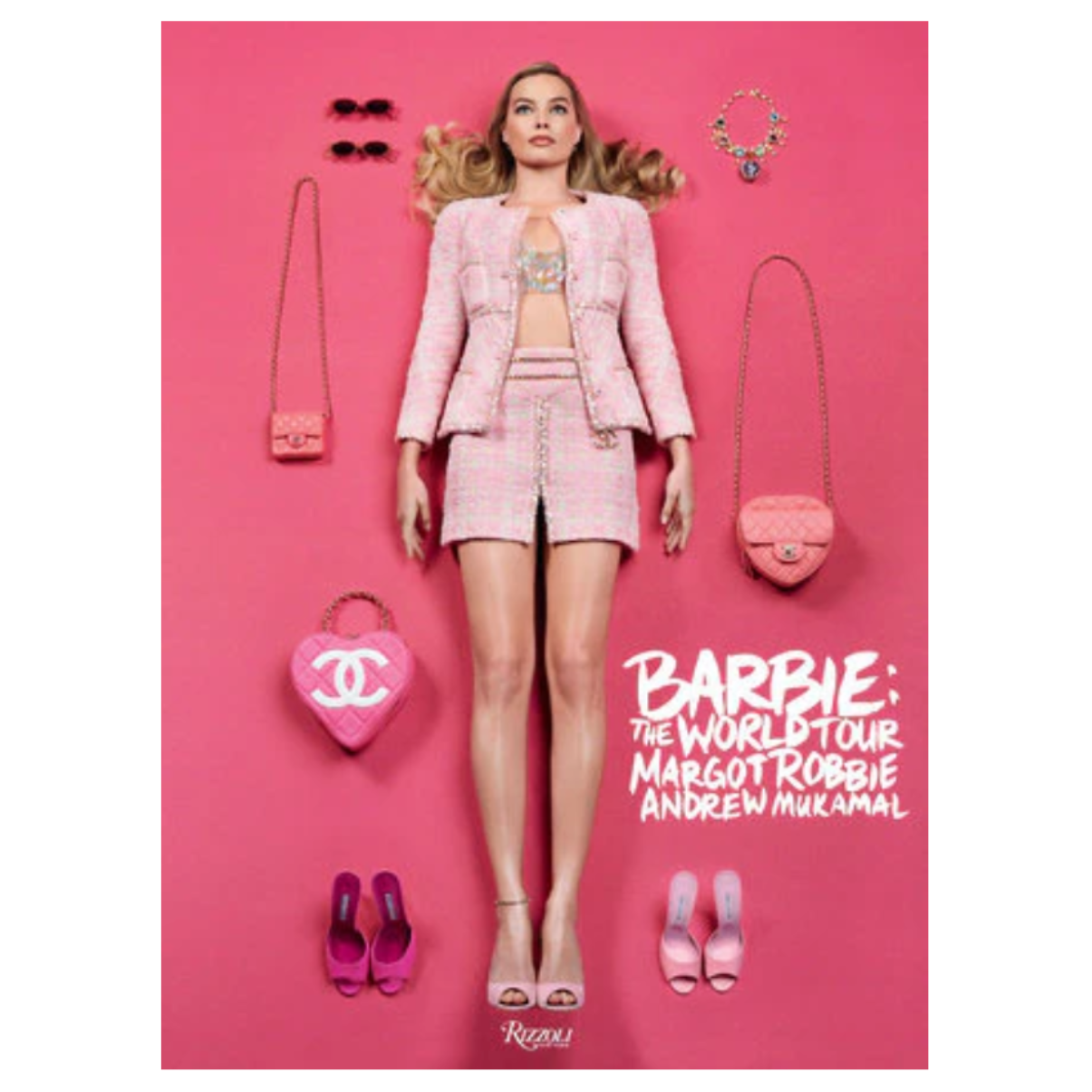 A fashion book for 'Barbie: The World Tour' featuring a model dressed in a pink blazer and shorts, surrounded by pink accessories including a Chanel heart-shaped bag, sunglasses, and heels, on a solid pink background.