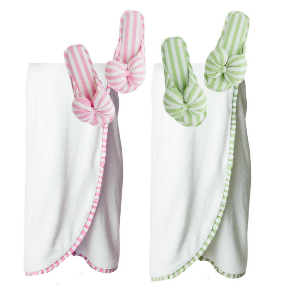 Two baby swaddle blankets on a white background, one with pink and white stripes and a pink border, and the other with green and white stripes and a green border, each with a matching fabric bow on the shoulder.