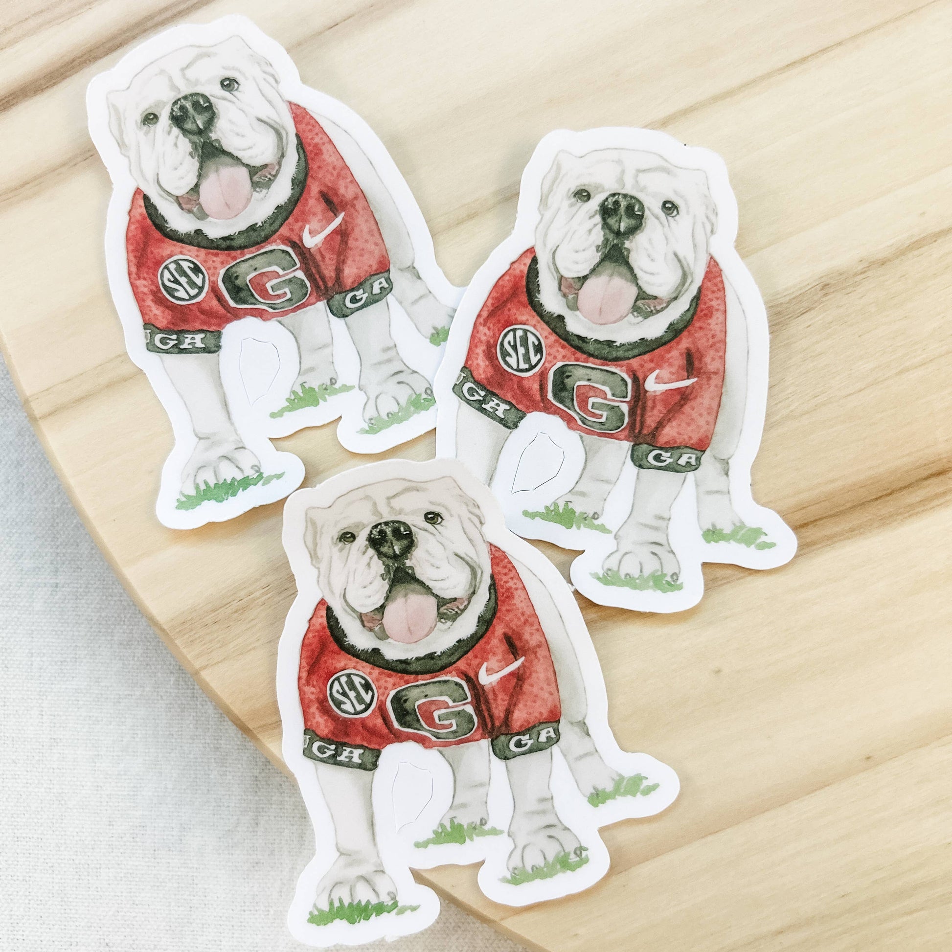 Three stickers of a bulldog in a red jersey on a wooden surface