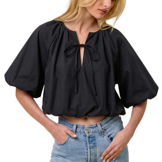 A woman wearing a black puff-sleeve crop top with a tie keyhole neckline, paired with light blue jeans, shown against a plain white background.
