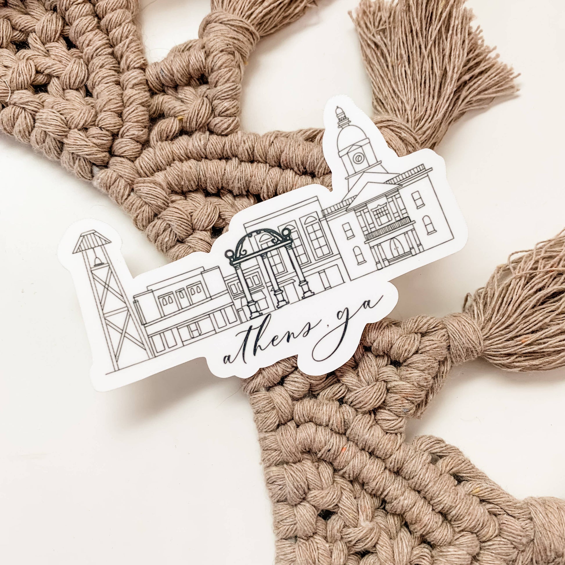 Sticker of a building with 'Athens, GA' text on a macrame wall hanging.