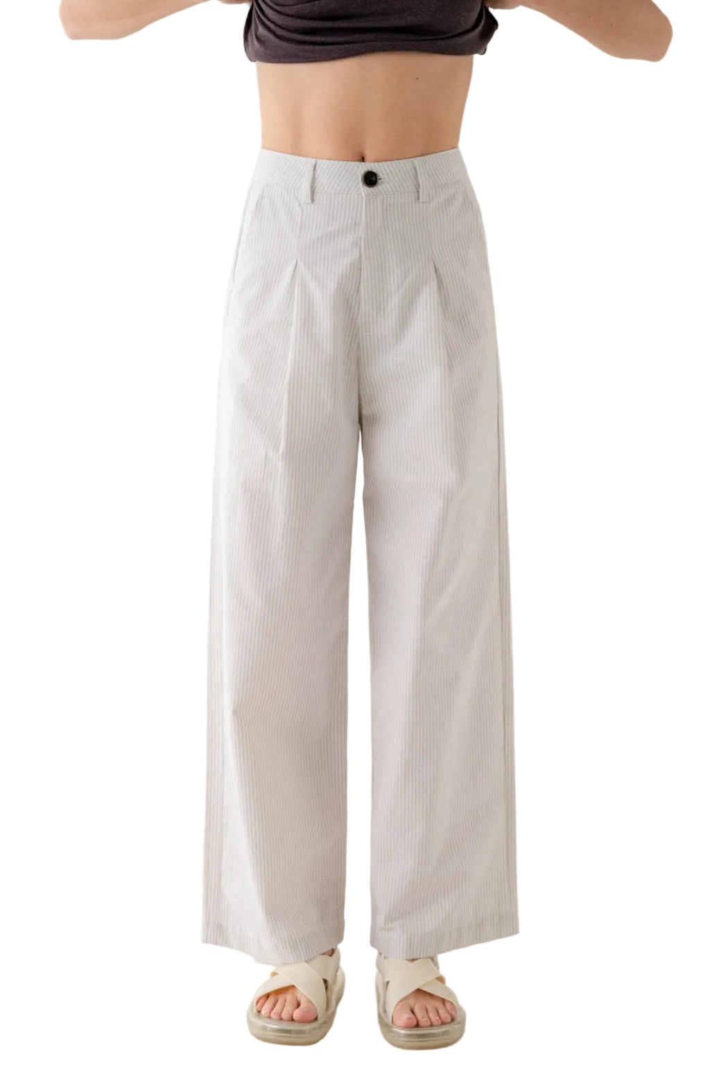 A person wearing high-waisted, wide-leg trousers in a light off-white or cream color, paired with a dark crop top and beige sandals, shown against a plain light background.