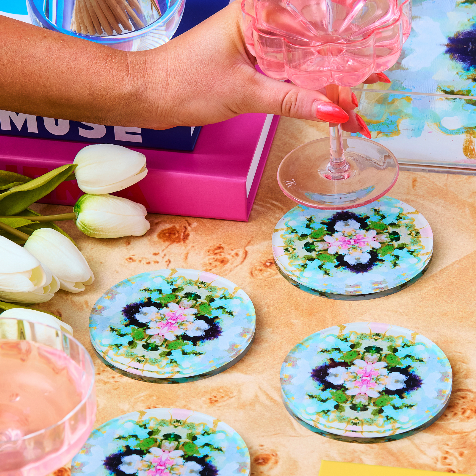 Decorative coasters with floral designs on a table with tulips and a pink box.