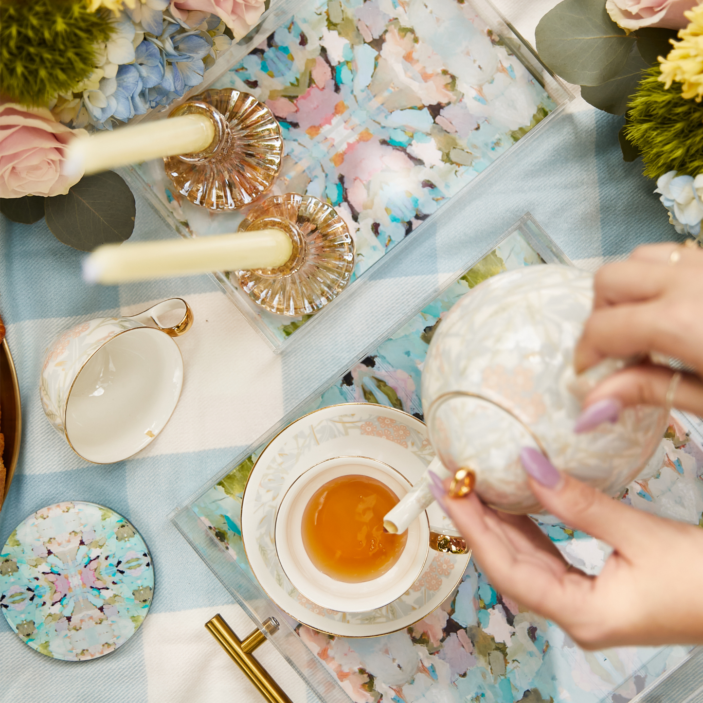 Tea cup with a saucer on a decorative tablecloth with flowers and candles.