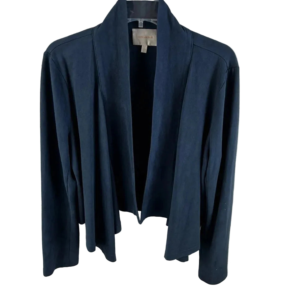 A dark navy blue open-front cardigan jacket with long sleeves, hanging on a black hanger against a white painted brick wall.