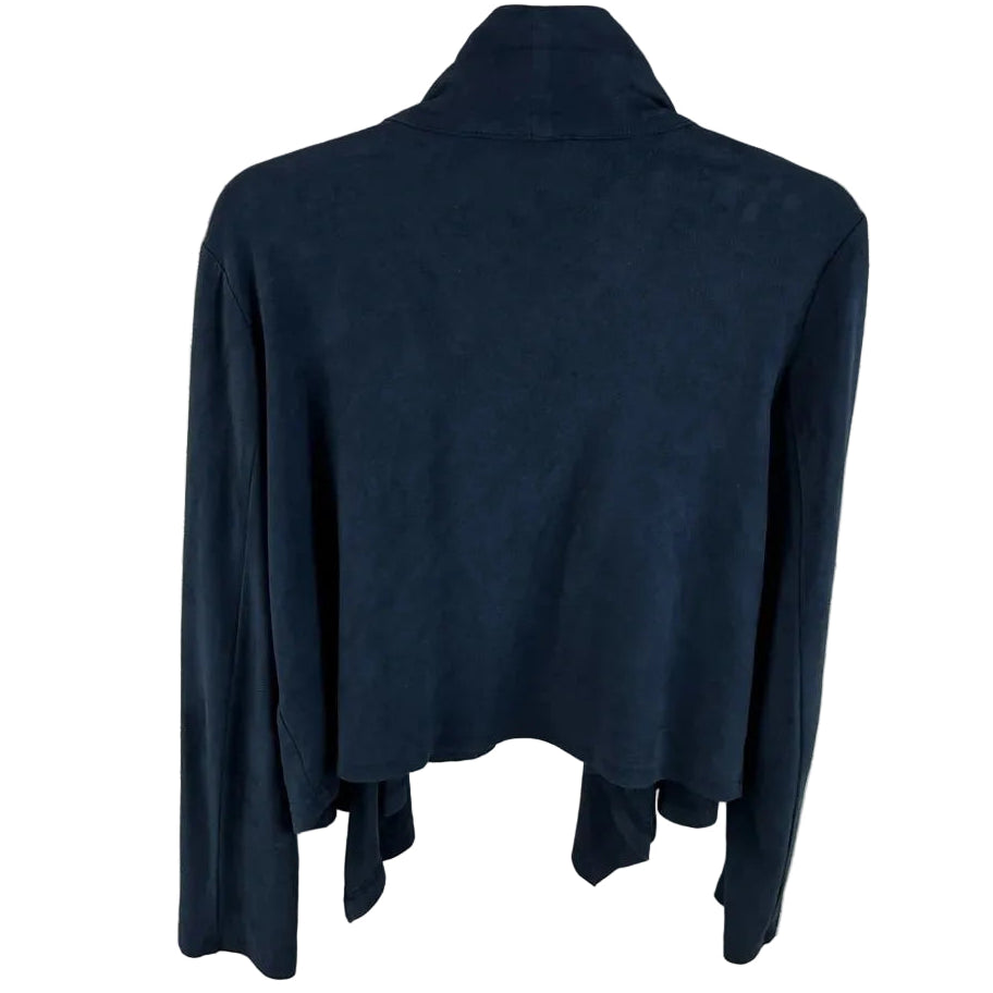 A dark navy blue long-sleeve turtleneck top hanging on a wire hanger against a white painted brick wall.